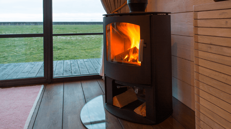 Will a log burner save you money; a lit log burner next to a basket of wood, used to save money on heating.